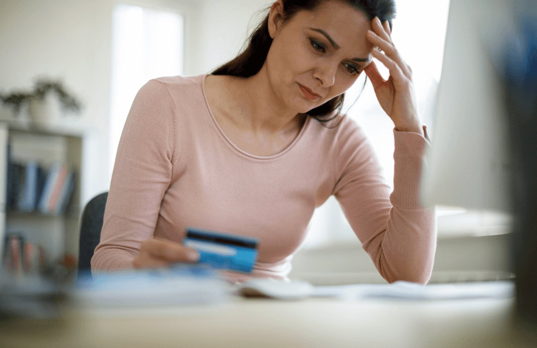 Woman with laptop holding credit card looking discouraged